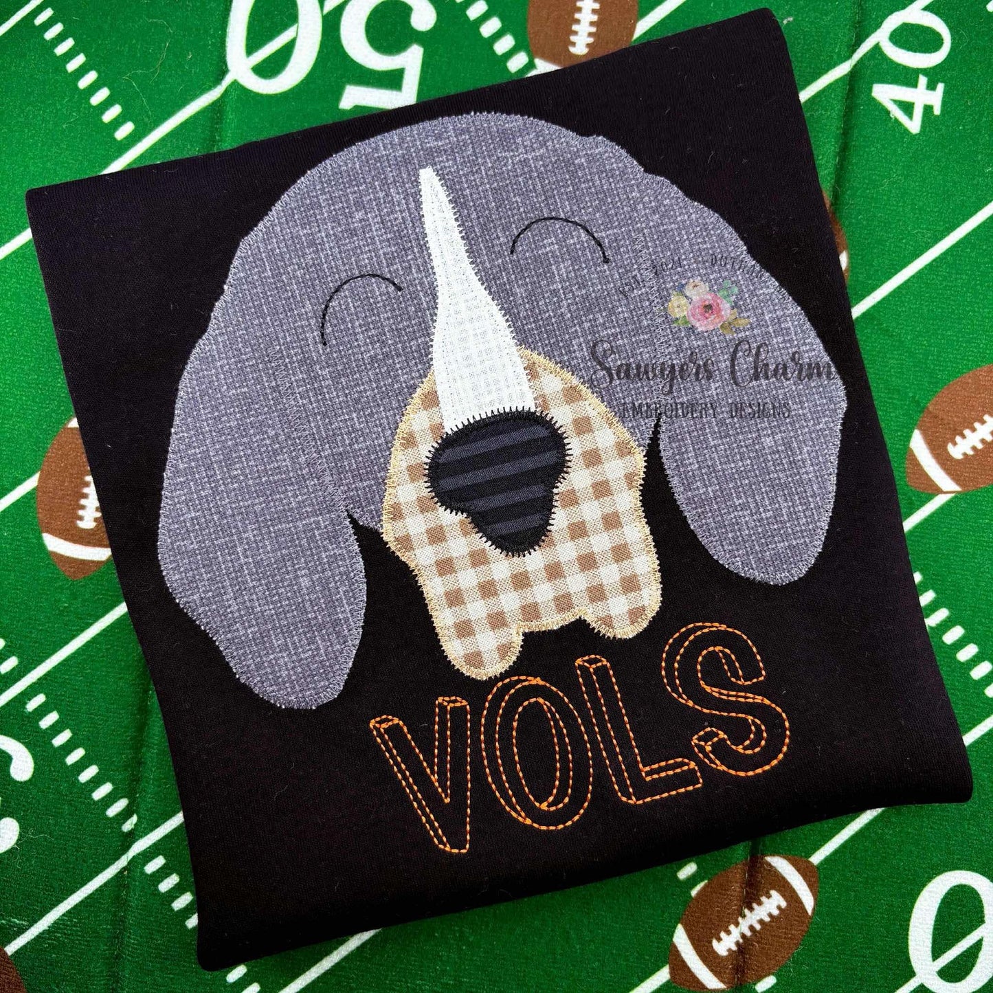 Embroidered patch of a dog with 'VOLS' on a black background, placed on a football field background.