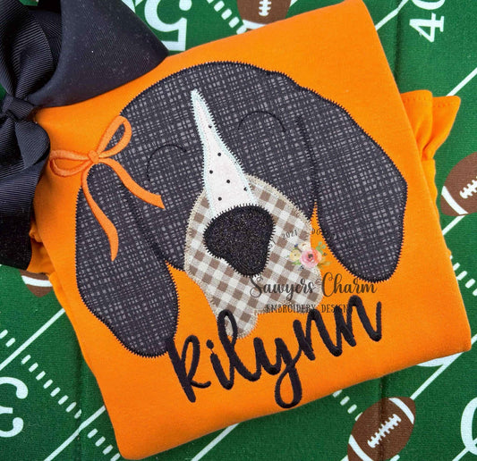Orange shirt with a dog patch and 'Kilynn' embroidery on a sports-themed background